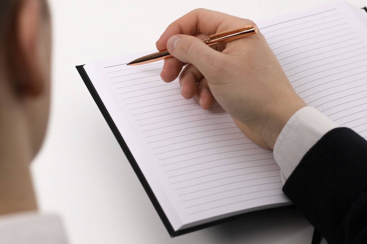 A business professional pauses over a lined notebook while documenting work that should move from memory into a system.