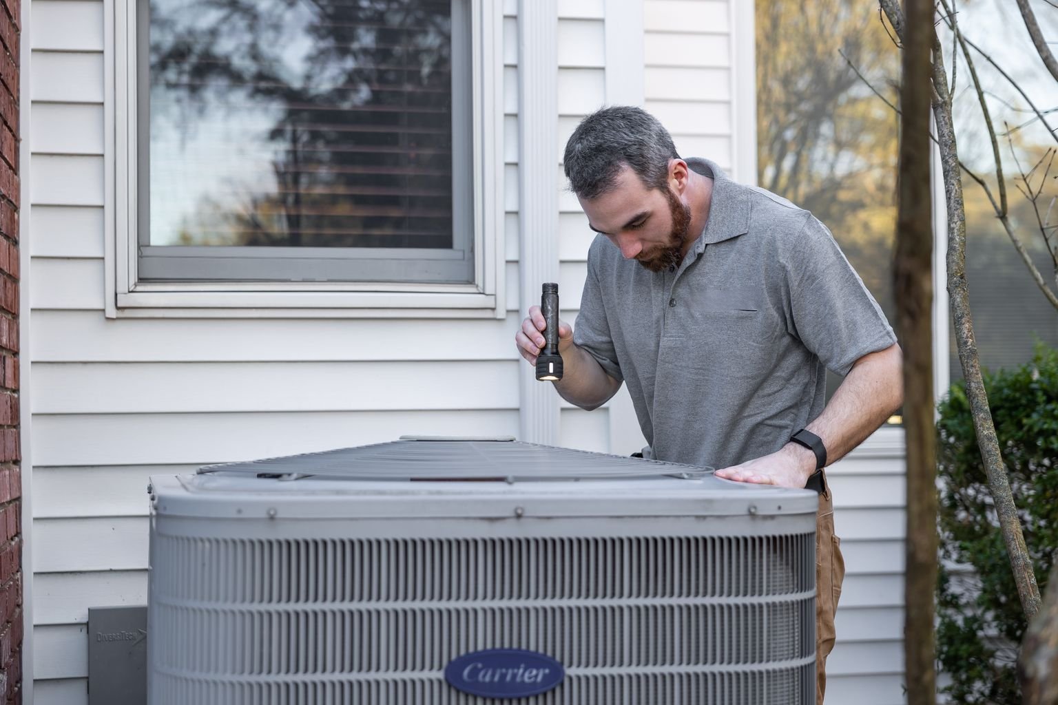 A maintenance technician inspects an outdoor HVAC unit while documenting the condition before closeout.